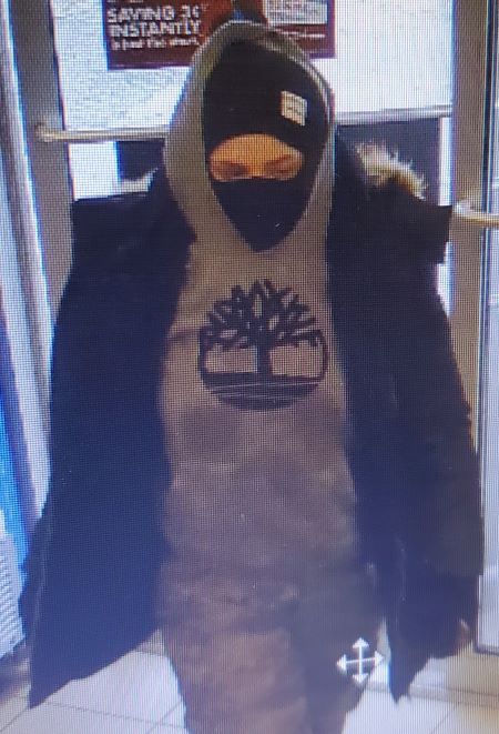 Une femme qui porte un masque, une veste fonc&eacute;e et un chandail gris dont le logo est un arbre noir et un cercle.